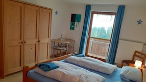 A room with two beds, a wooden wardrobe, a small table with a chair, and a window with curtains. - Ihr Ferienhof am Rande der Alpen (Seeg)