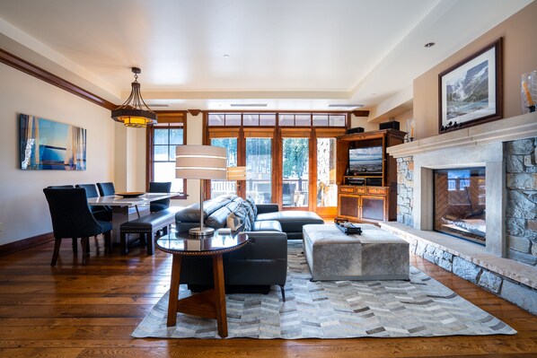 A spacious living room with a fireplace, a dining area, and a large window offering a view of the outdoors.