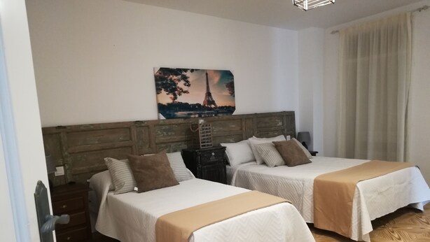 Een hotelkamer met twee bedden, houten hoofdeinden, een schilderij van de Eiffeltoren en een houten parketvloer.