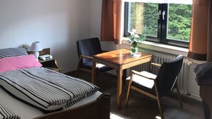 A hotel room with a bed, a wooden table with chairs, a window with curtains, and a radiator. - Quite double rooms with breakfast (Hornberg)