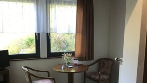 A small room with two wooden chairs around a round table, a window with curtains, and a door. - Quite double rooms with breakfast (Hornberg)