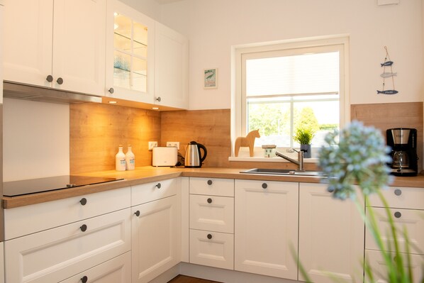 A modern kitchen with white cabinets, a wooden countertop, a sink, and a window.