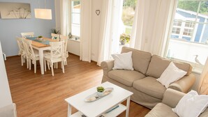 Een moderne woonkamer met een beige bank, een witte salontafel en een eettafel met stoelen.