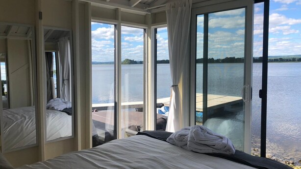 A hotel room with a large sliding glass door leading to a balcony overlooking a lake. - Glamping at the Cabana! (Wendover, On)