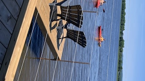 A wooden dock with two kayaks and a person paddling in the background. - Glamping at the Cabana! (Wendover, On)