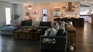 Ein modernes Wohnzimmer mit einem Ecksofa, einem Couchtisch und einem Essbereich, im Hintergrund eine Küche.