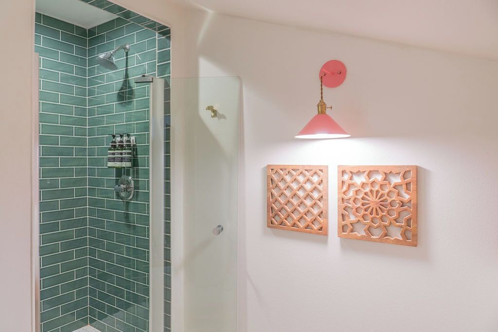 Ducha con azulejos verdes, puerta de cristal y una lámpara colgante rosa.