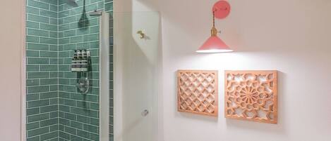 Ducha con azulejos verdes, puerta de cristal y una lámpara colgante rosa.