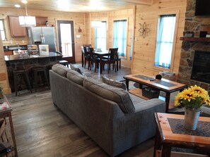 A cozy cabin interior with a sofa, dining table, chairs, a kitchen area, and a fireplace.
