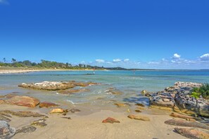 A beach with clear water, rocks, and a distant view of a lighthouse.