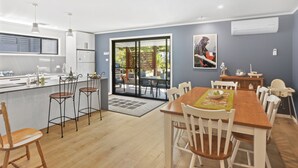A modern kitchen with a dining area, featuring a large island, bar stools, and a view through the glass door to the outside.