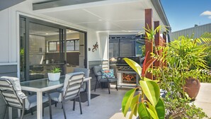 A patio with a glass table and chairs, a grill, and potted plants.