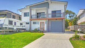 A two-story modern house with a balcony, a garage, and a driveway.