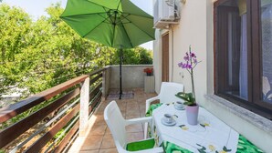 A balcony with a green umbrella, white chairs, a table with a floral tablecloth, and a potted orchid. - Lovely apartment in Valbandon with WiFi (Valbandon)