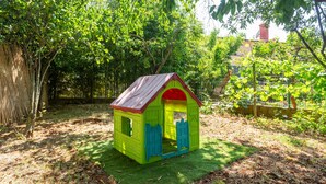 A small, colorful playhouse with a red roof and green walls, situated in a garden with trees and a fence in the background. - Lovely apartment in Valbandon with WiFi (Valbandon)