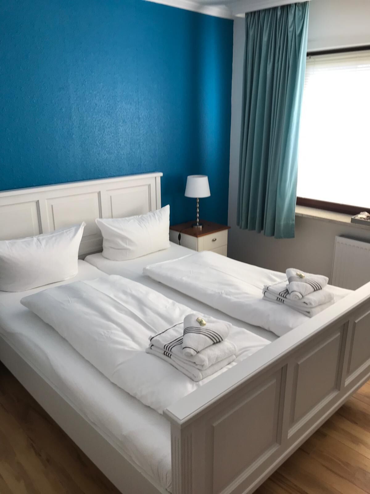 Un lit double avec du linge de lit blanc, une table de chevet avec une lampe et une fenêtre avec des rideaux.