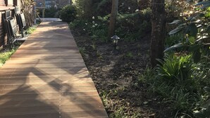 Een houten pad dat leidt naar een gebouw met een bakstenen gevel, omgeven door groen en bomen.