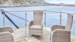Una terraza con sillas de mimbre que da a un cuerpo de agua, una costa rocosa y un cielo despejado.