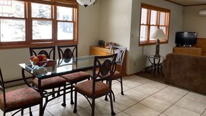 Un comedor con mesa de vidrio, cuatro sillas, una lámpara de araña y un televisor en una esquina.