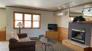 Una sala de estar con un sofá, una mesa de centro de vidrio, un televisor, una chimenea y una ventana con persianas.