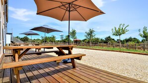 A wooden deck with picnic tables and umbrellas, surrounded by a gravel area and a wooden fence. - Cozy home in Méjannes-le-Clap (Méjannes-le-Clap)