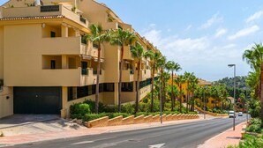 A multi-story hotel with balconies, palm trees, and a clear view of the sea.