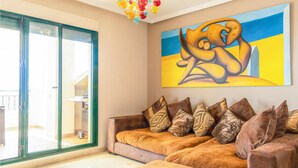 A living room with a sofa set, a large abstract painting, and a glass door leading to an outdoor area.
