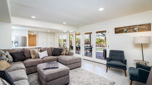 Ein modernes Wohnzimmer mit einer Eckcouch, einem Hocker und einem Essbereich mit Gartenmöbeln.