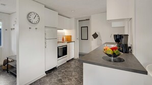 A modern kitchen with white cabinetry, a built-in oven, a refrigerator, and a stone-tiled floor.