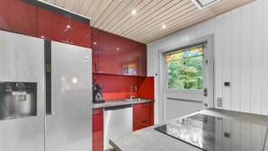 Ett kompakt kök med ett kylskåp i rostfritt stål, en kaffebryggare och ett fönster med utsikt över grönområden.