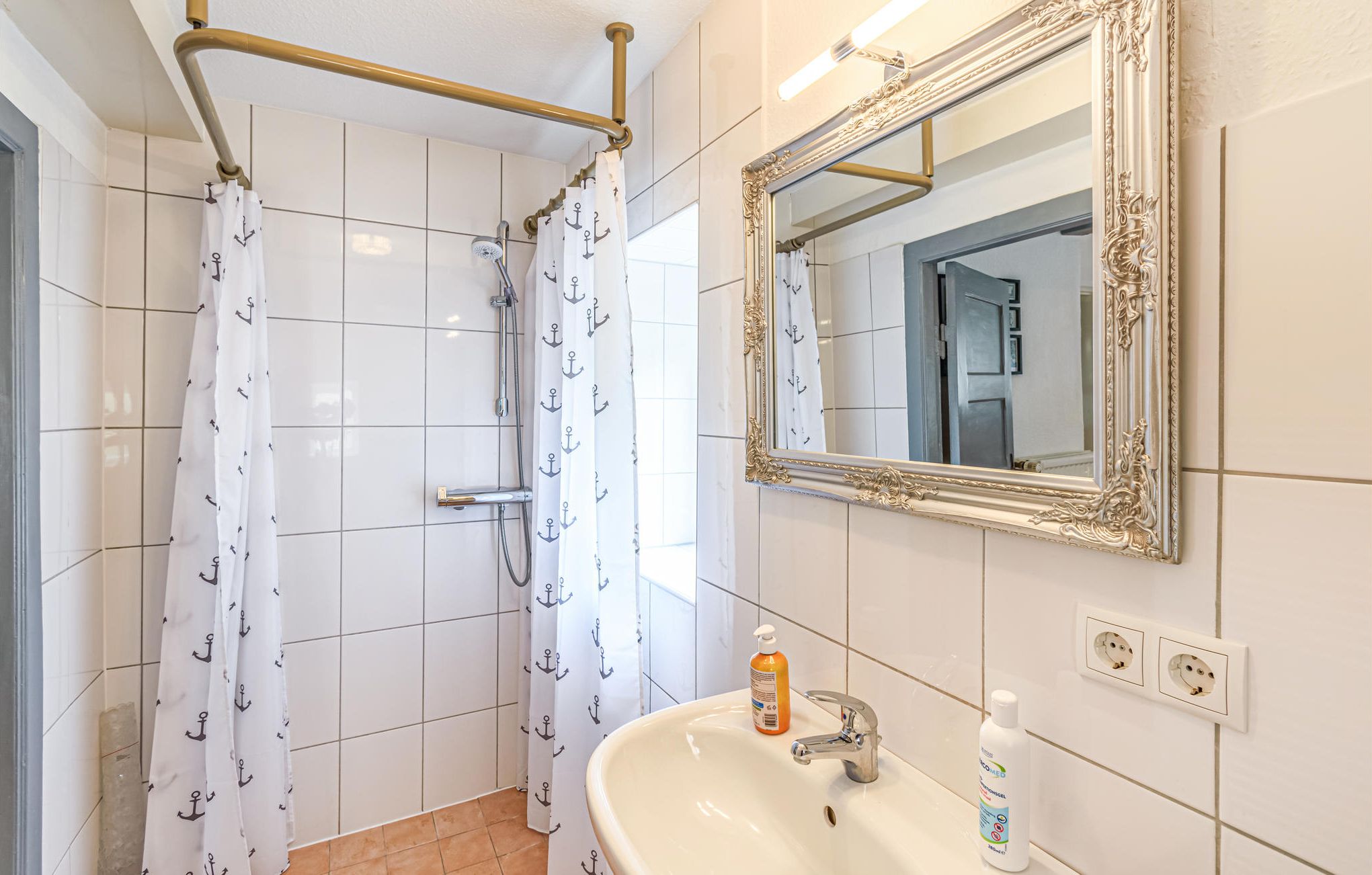 Een badkamer met een douche, een wastafel, een spiegel en een fles handzeep.