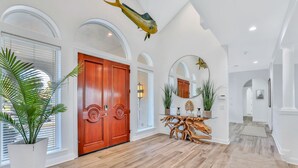 Un pasillo amplio con suelo de madera, una puerta de madera grande y una mesa de madera con plantas.