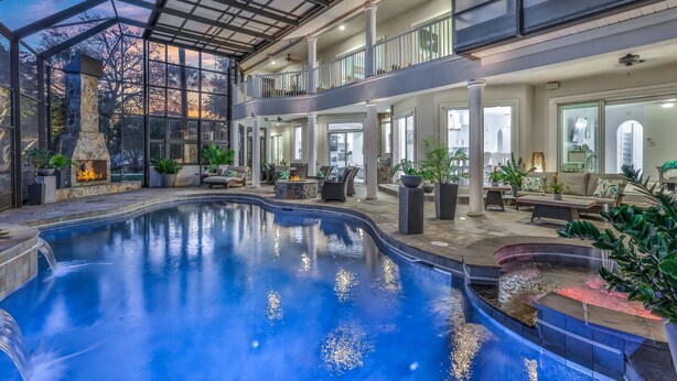 Un área de piscina interior espaciosa con techo de cristal, varias zonas de estar y chimenea de piedra.