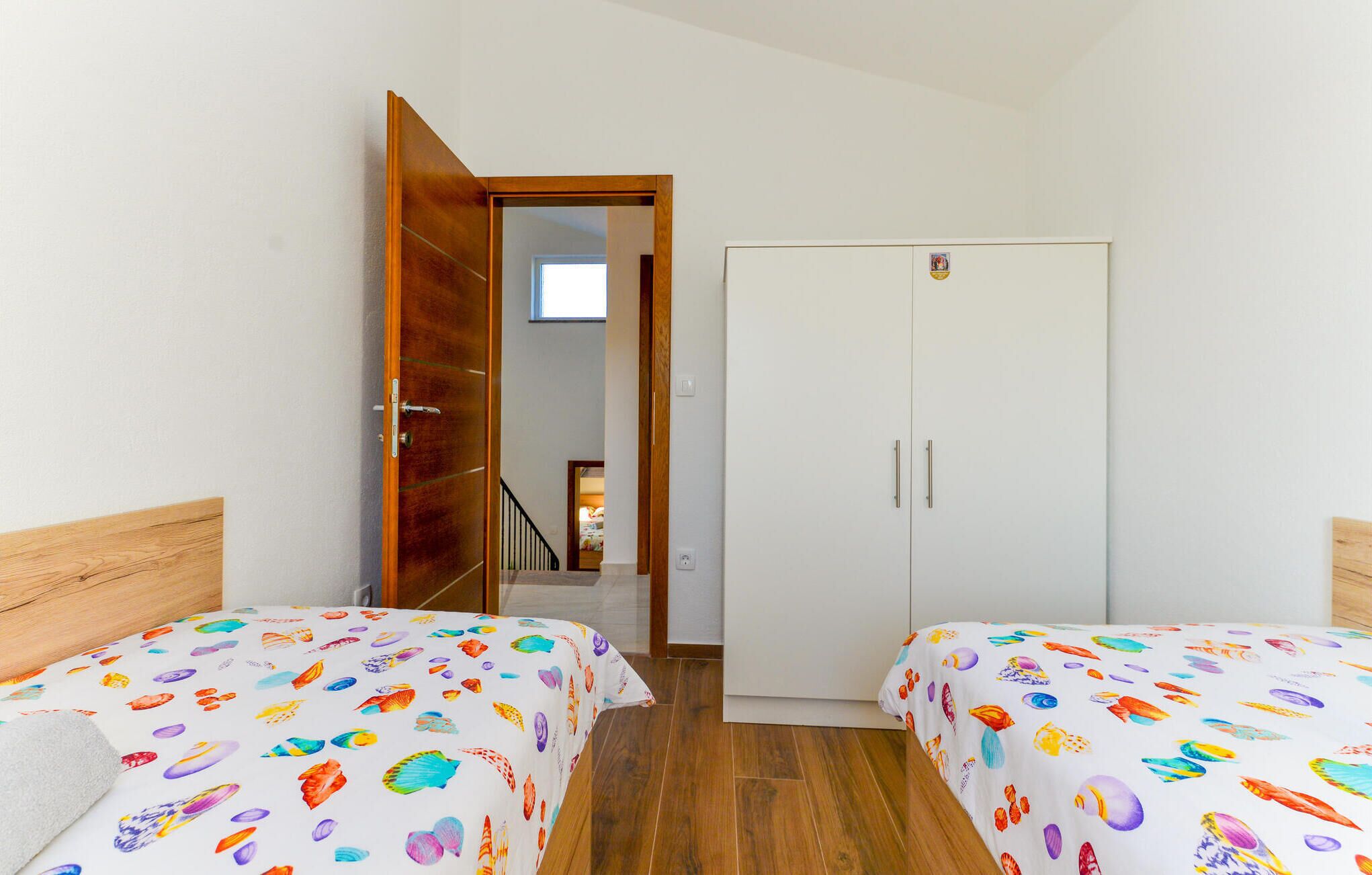 A bedroom with two beds, a wardrobe, and a door leading to a staircase.