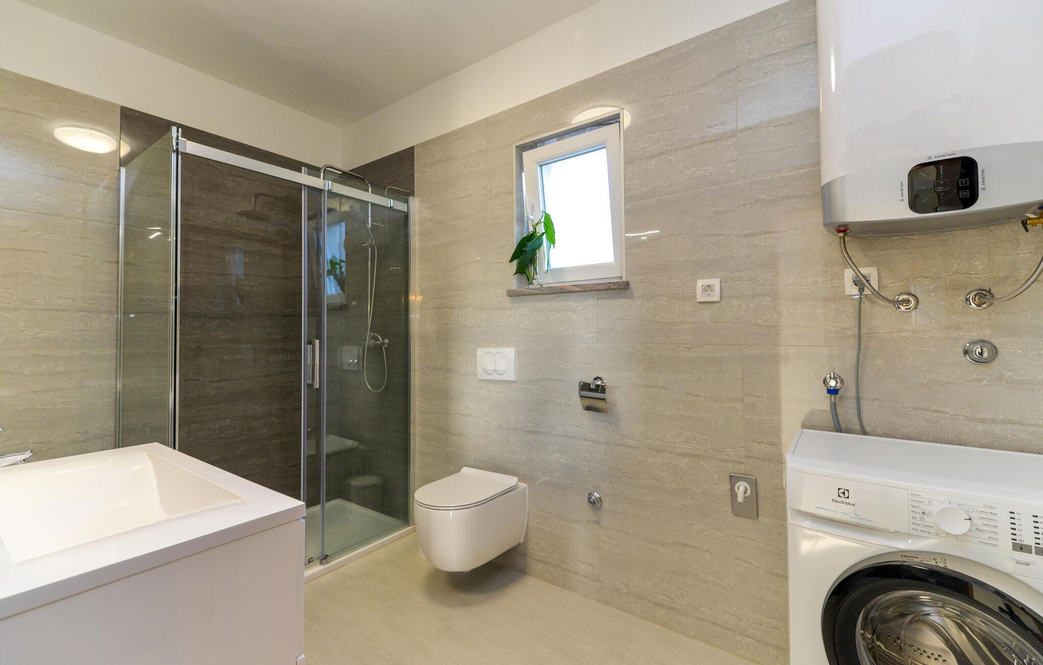 Une salle de bain moderne dotée d’une douche à parois de verre, de toilettes, d’un lavabo et d’un lave-linge encastré.