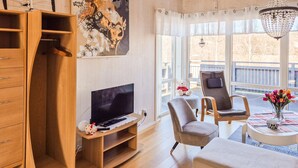 A modern living room with a TV, wooden furniture, a chair, a table with a vase, and a balcony view. - 2 bedroom amazing home in åsensbruk (Åsensbruk)