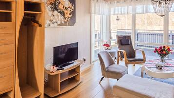 A modern living room with a TV, wooden furniture, a chair, a table with a vase, and a balcony view.