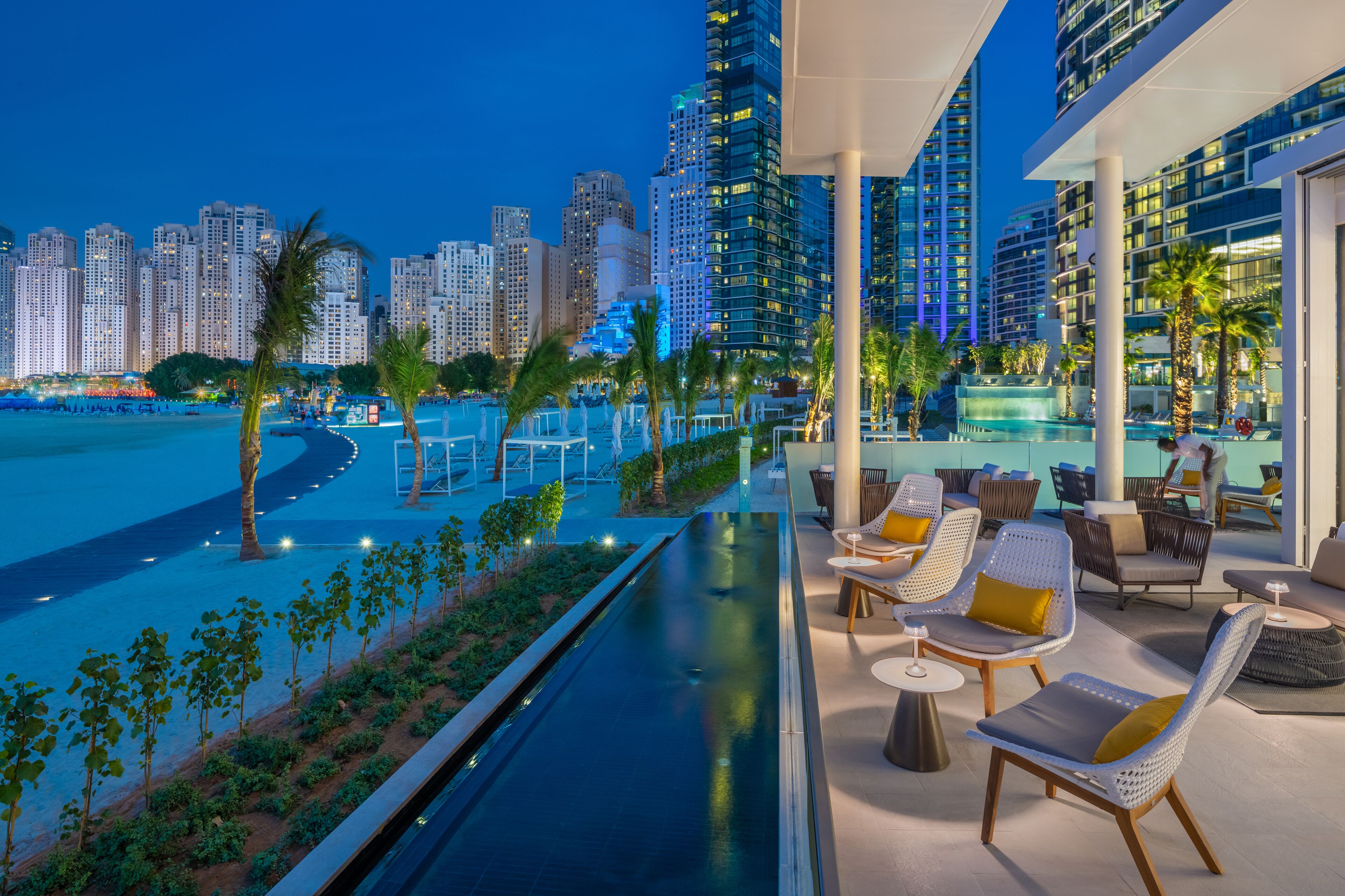 A rooftop pool area with lounge seating, a view of the city skyline, and a pathway leading to the pool.