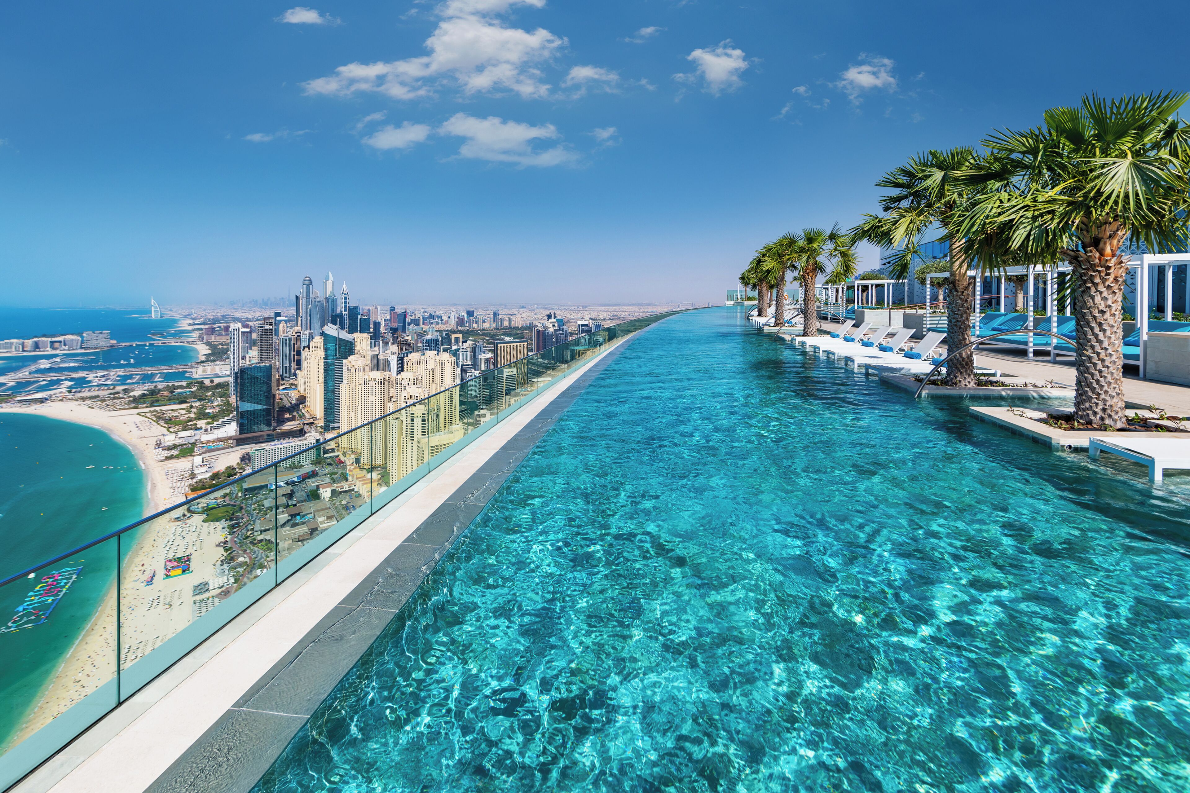 Ein klares, blaues Infinity-Pool mit Blick auf die Skyline, Palmen und Liegestühle.