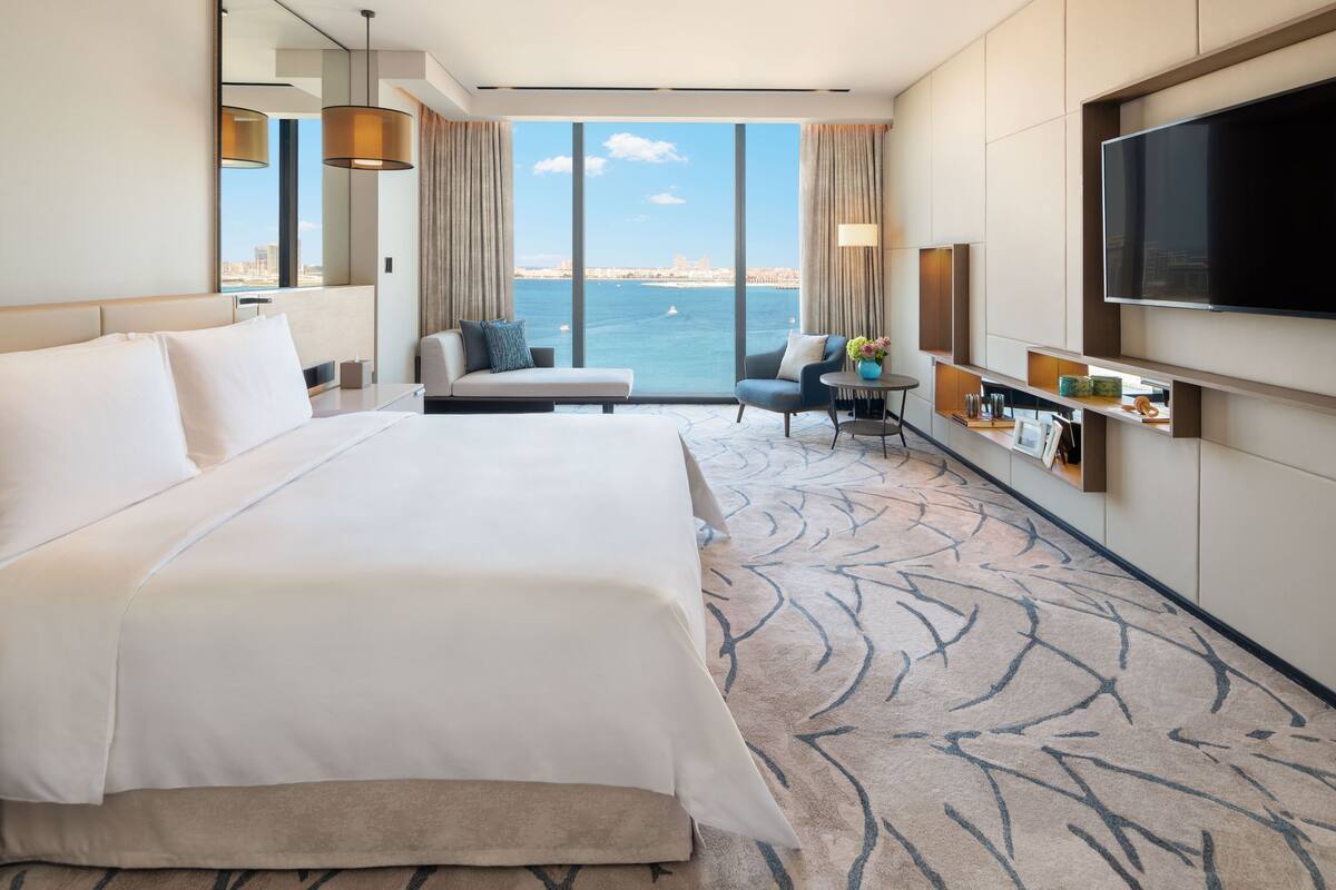 A hotel room with a large bed, a sofa, a TV, and a view of the sea.