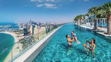 Escena junto a la piscina con vista a la ciudad, palmeras y una playa.