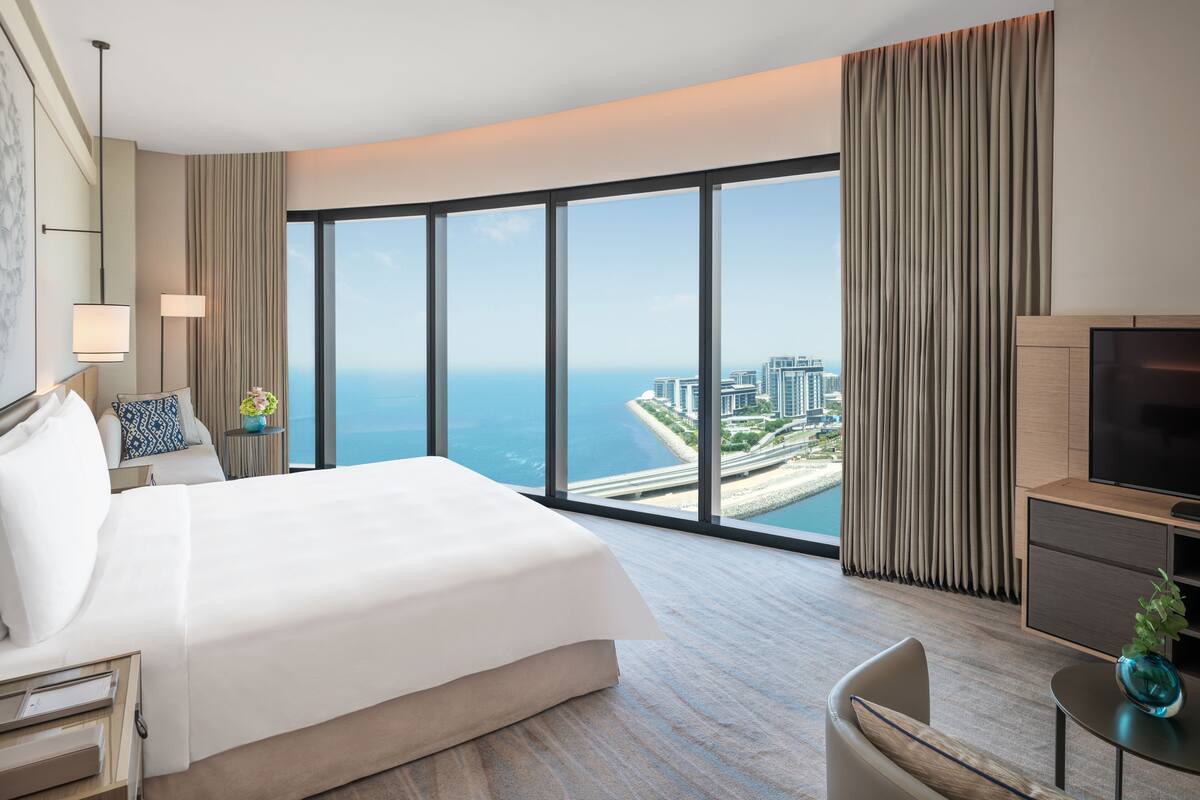 A hotel room with a large bed, a TV, and a view of the city and ocean.