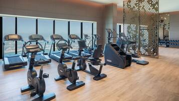 A gym with various exercise machines, large windows, and a view of a cityscape.