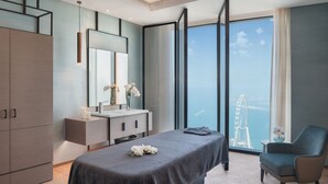 A modern hotel room with a large bed, a sitting area, a vanity with a mirror, and a view of a Ferris wheel. - Address Beach Resort (Dubai)