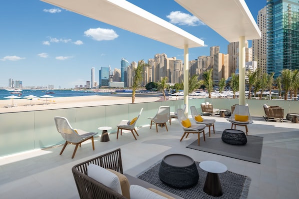 Un salon sur le toit offrant une vue panoramique sur la ville, avec des espaces de détente en plein air et un coin aménagé près de la piscine.