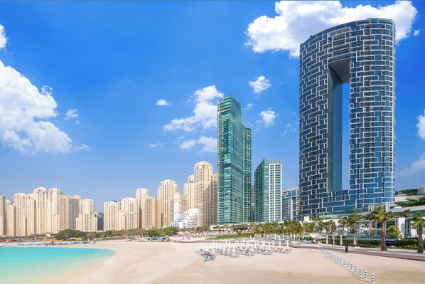 A beachfront hotel with modern architecture, a sandy beach, and a clear blue sky. - Address Beach Resort (Dubai)