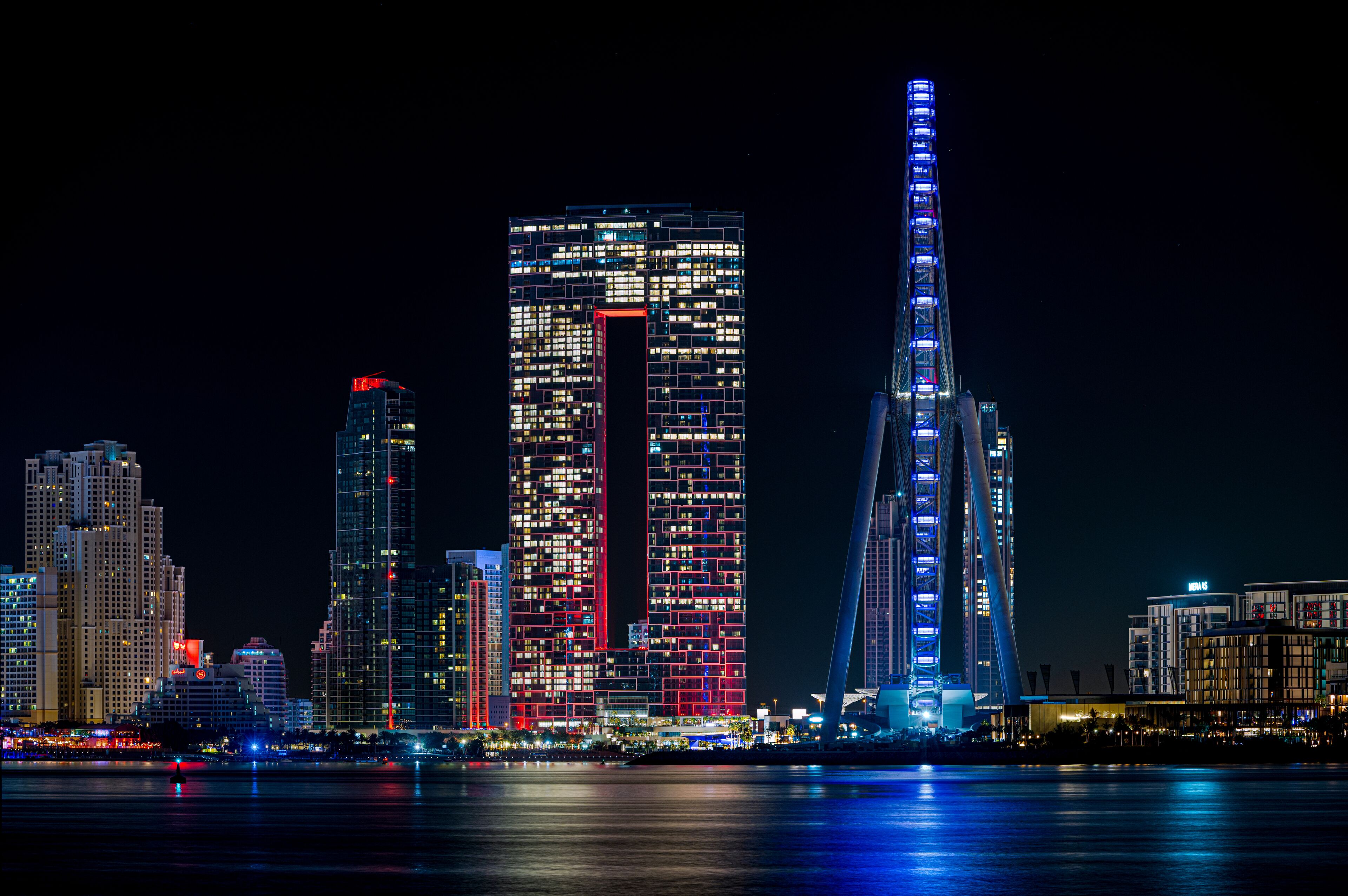 A city skyline at night with illuminated buildings and a prominent bridge.