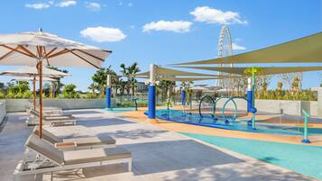 A rooftop pool area with lounge chairs and umbrellas, a water feature, and a Ferris wheel in the background.