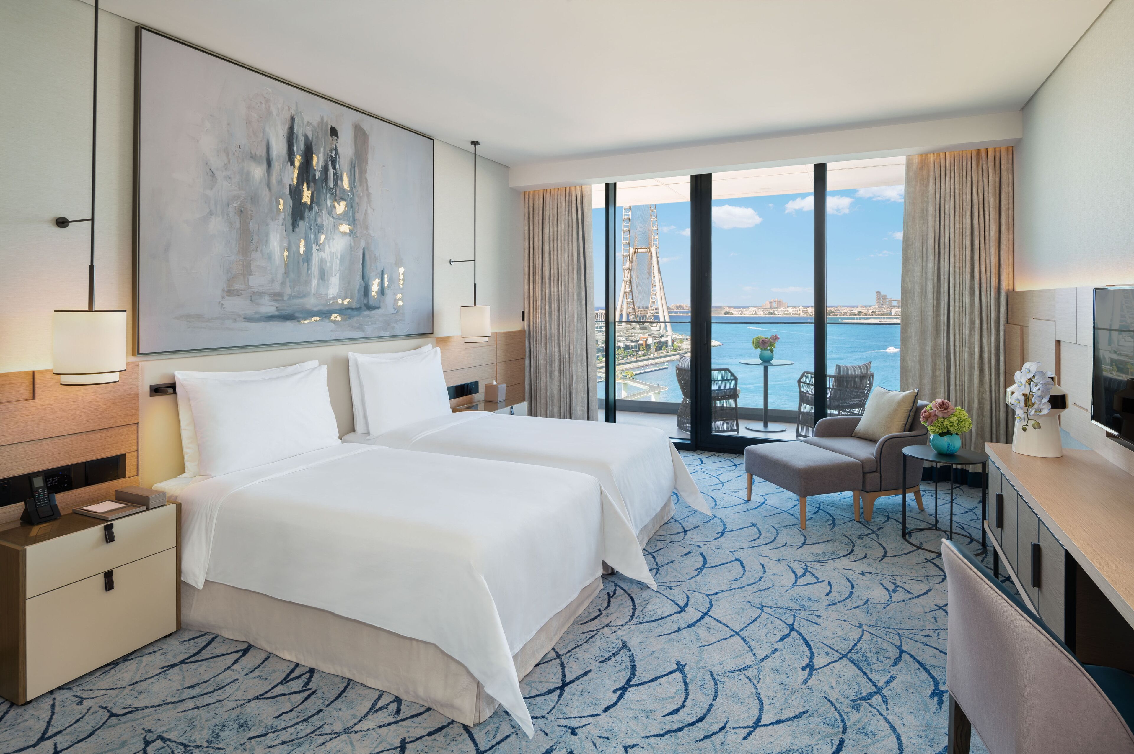 A hotel room with two beds, a large window with a view of a bridge and water, a desk with a TV, and a chair.