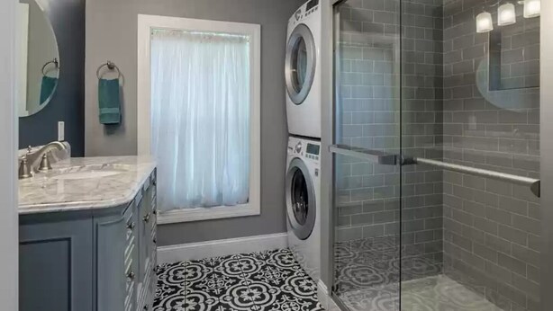 A modern bathroom with a built-in washing machine, a glass shower enclosure, and a patterned floor. - *New* The Foundry Getaway 2BR / 1 BR (Saranac Lake)